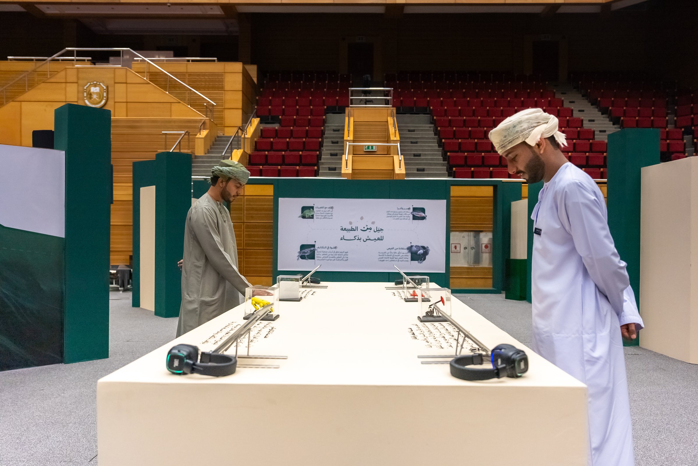 Two students inspect entries laid out on a display table in a large auditorium.