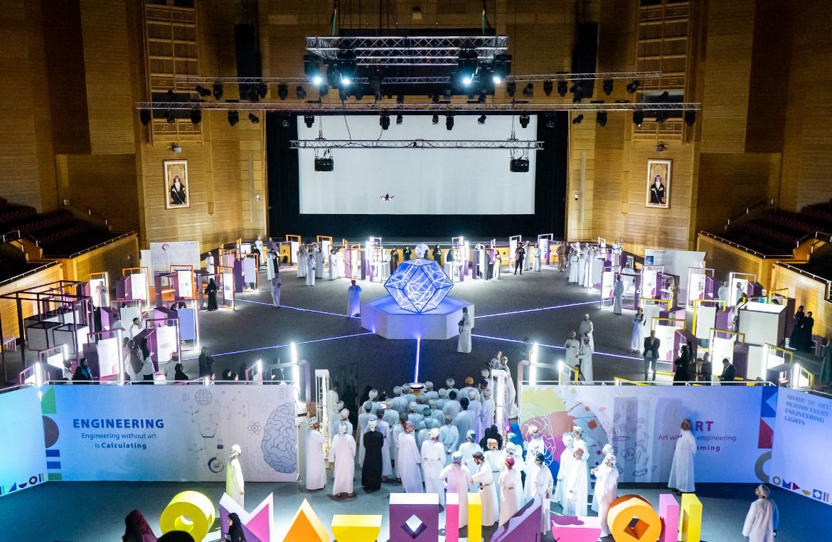 An exhibition hall: visitors walk between lit display panels around a glowing geometric sculpture.