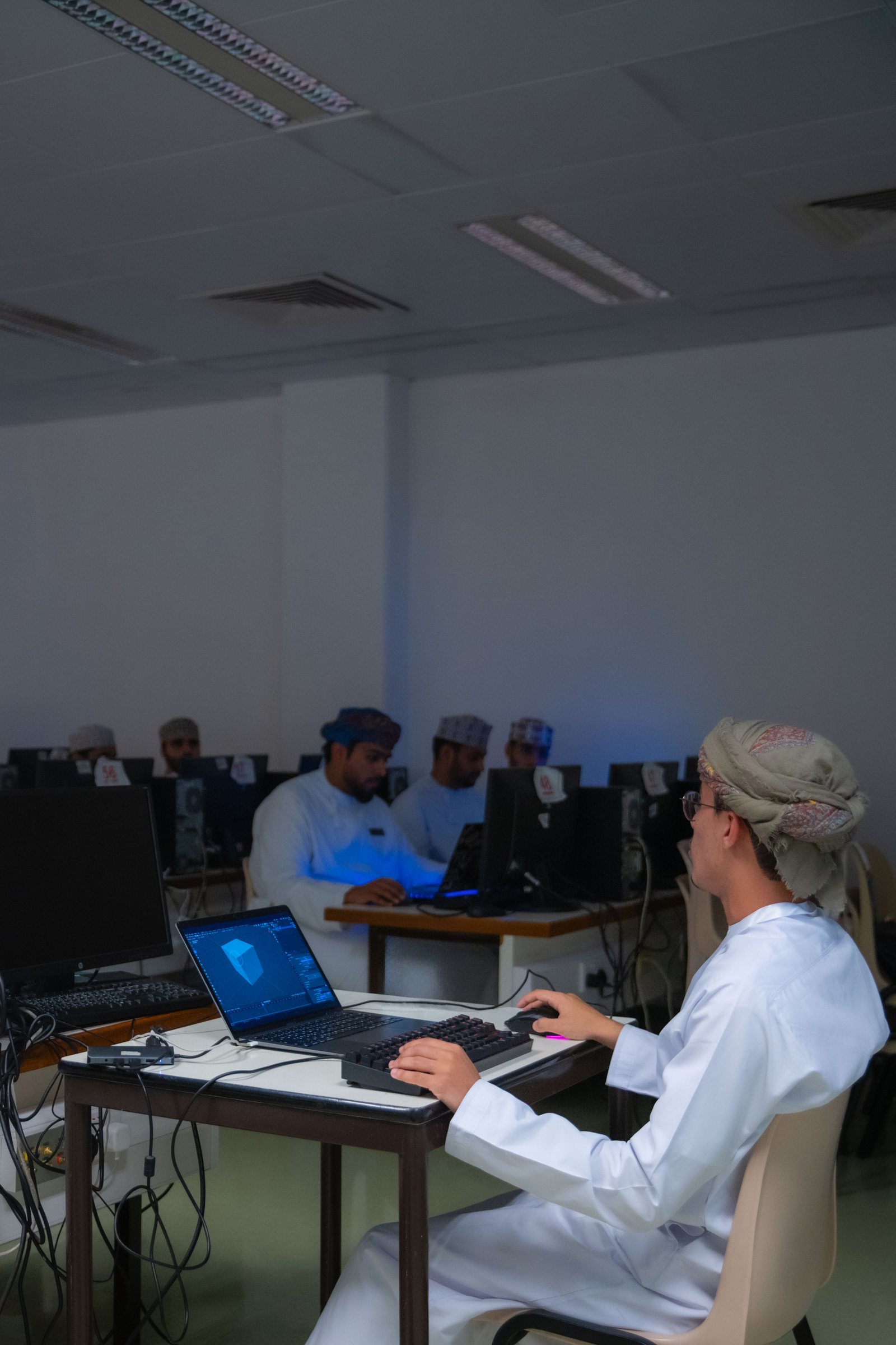 Students working at computers in a lab; in the foreground, one models a 3D shape on a laptop.