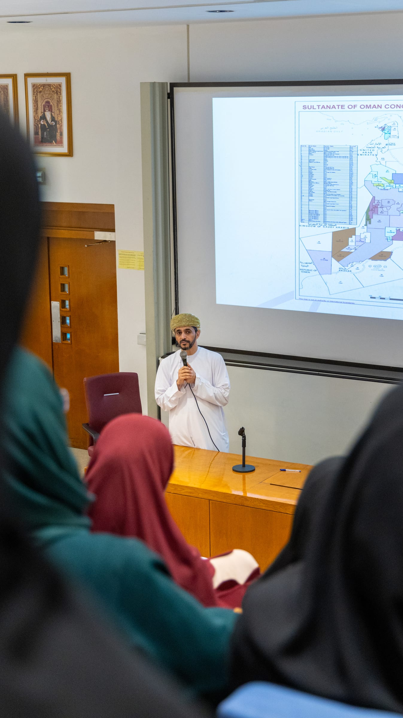 A speaker with a microphone presents a map of Oman’s concession areas to the audience.